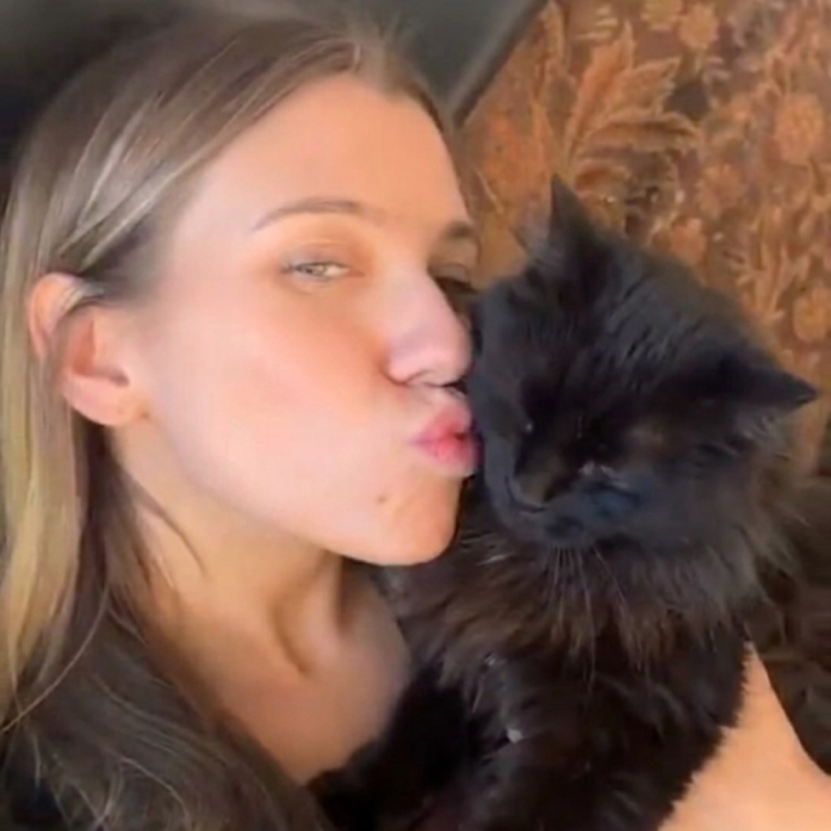 A woman holding her long haired black cat close and kissing the side of his head.